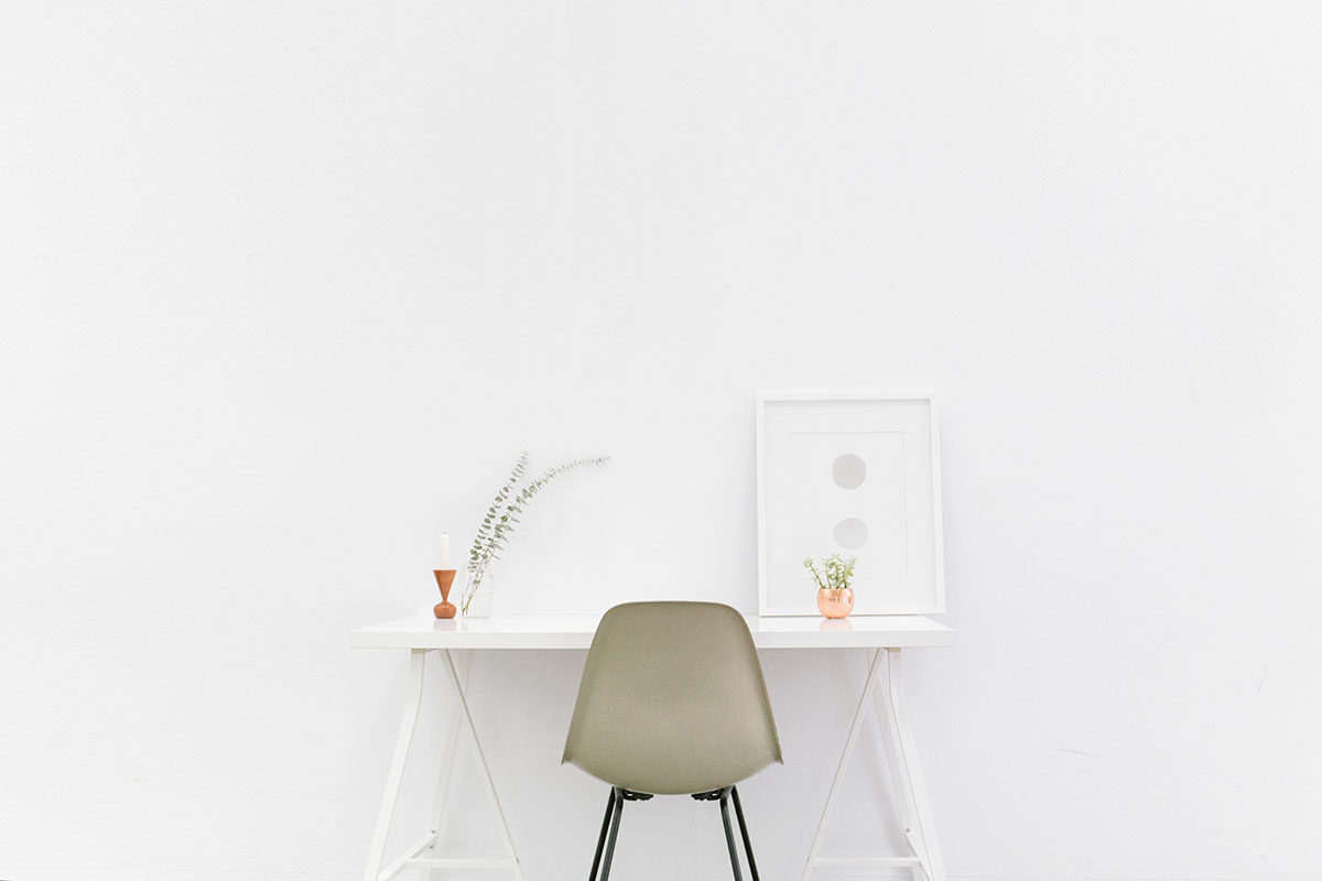 Minimalist workspace with white desk and chair against a plain wall.