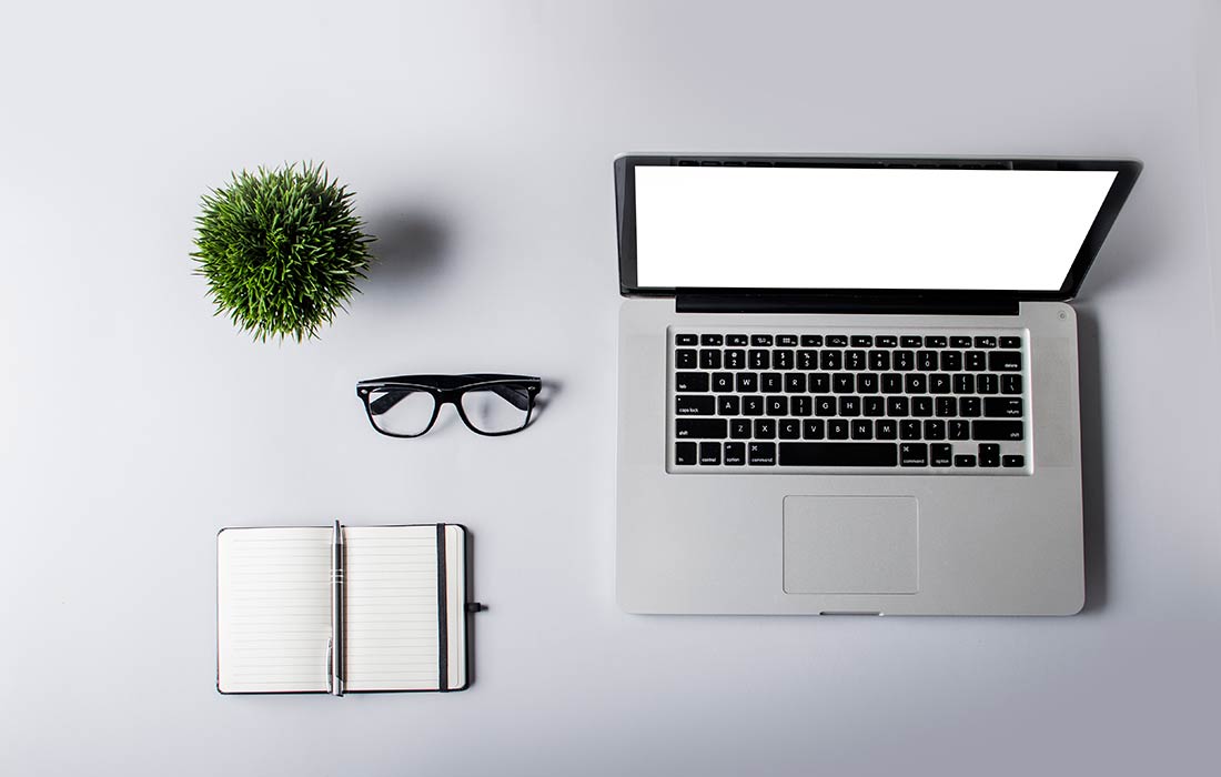 Laptop, notebook, glasses, and plant on desk.