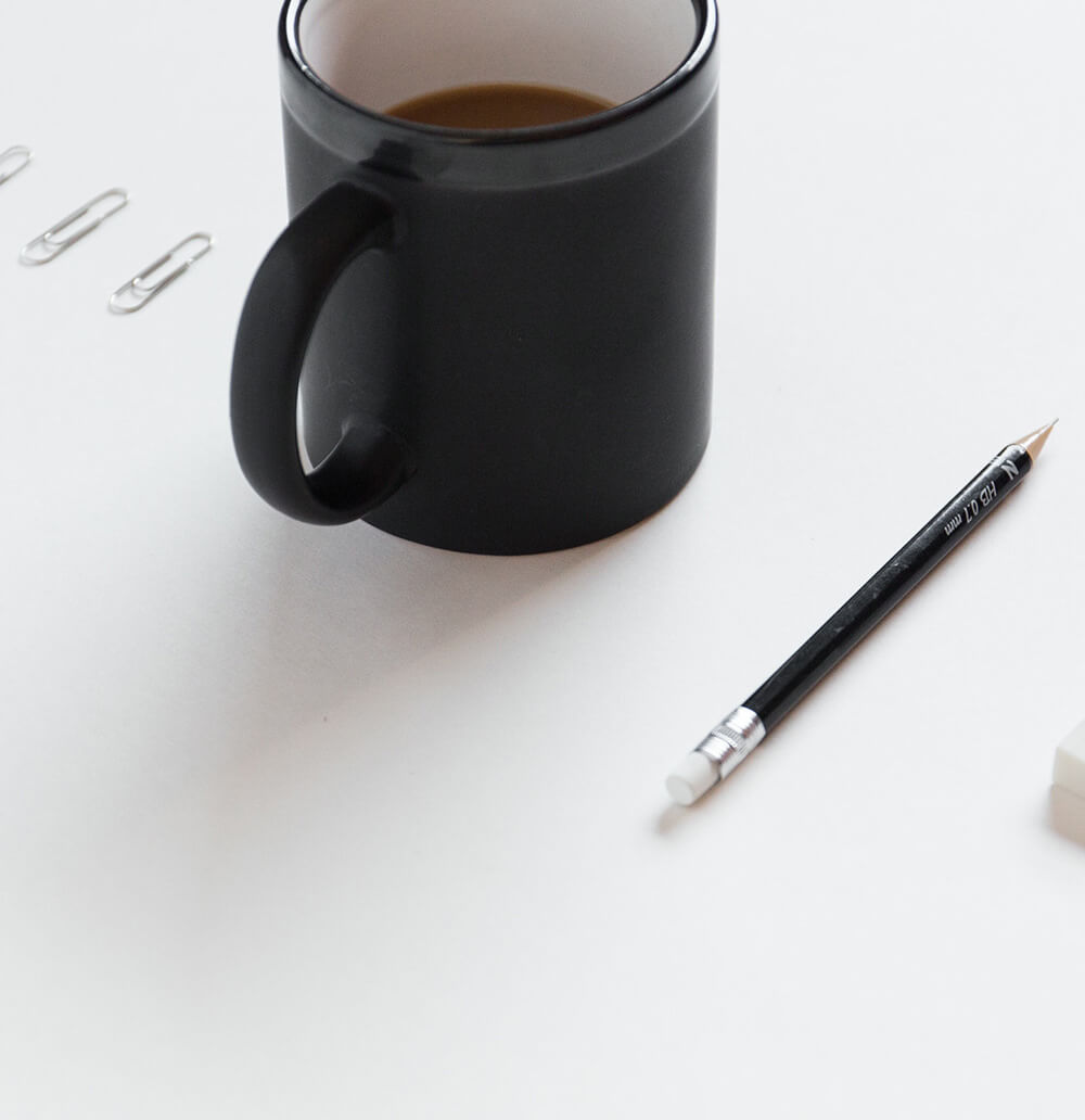 Black mug, pencil, paperclips on white desk.