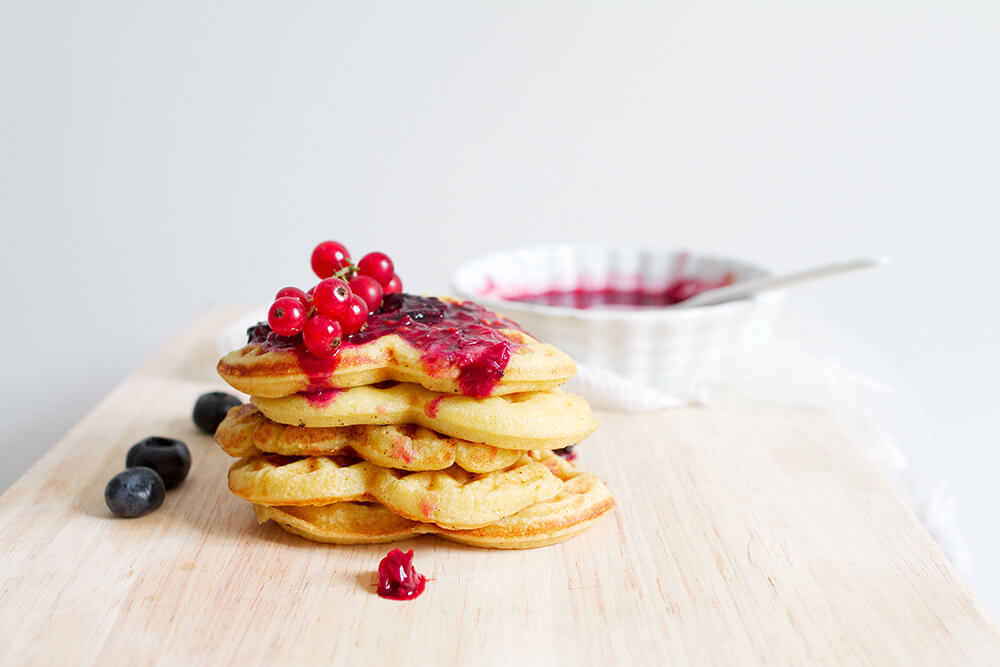 Stack of heart-shaped waffles topped with red currants and jam.