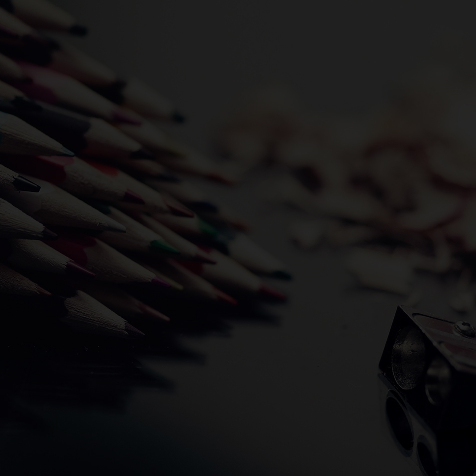 A collection of colored pencils and a sharpener on a dark surface.