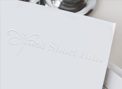 Embossed white card with elegant 'Real Short Hills' text and dragonfly logo.