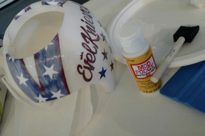 A patriotic-themed mug, Mod Podge glue, and a brush on a table.